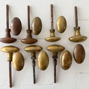 Peut inclure: Un ensemble de huit poignées de porte ovales et leurs tiges métalliques correspondantes. Le lot comprend quatre poignées avec tiges fixées et quatre poignées ovales détachées, présentant un mélange de finitions en laiton vieilli et brun.