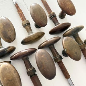 May include: A collection of antique oval-shaped brass door knobs with weathered, tarnished surfaces. Each knob features a central metal spindle, some showing visible rust, and a decorative collar detail where the handle meets the shaft.