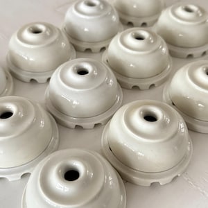 Puede incluir: Un conjunto de lámparas de techo de cerámica blanquecina. Cada lámpara tiene un diseño redondeado en forma de campana con un agujero central y una base circular. Las lámparas están dispuestas en una vista de cerca, desde arriba.