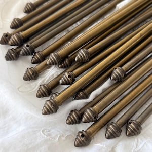 May include: A collection of antique brass rods with decorative, spiral-shaped finials. The rods are arranged diagonally, showcasing their aged patina and intricate detailing. The finials have a small hole. The rods are likely for a curtain rod or similar decorative purpose.