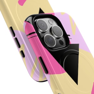 Könnte beinhalten: Nahaufnahme von zwei Handyhüllen. Die Hüllen haben ein farbenfrohes abstraktes Design mit rosa, gelben und schwarzen Formen. Die Handyhülle auf der rechten Seite ist fokussiert und zeigt die Kameralinsen und den schwarzen Rahmen.