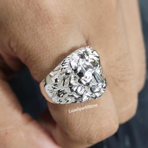 Könnte beinhalten: Ein silberfarbener Ring mit einem detaillierten Löwenkopf-Design. Der Ring hat eine strukturierte Oberfläche und wird am Finger getragen. Der Text "LuxeSparkStone" ist auf dem Ring sichtbar.