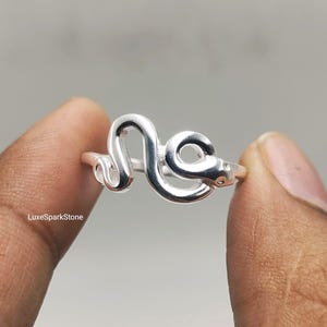 May include: A polished silver-toned ring featuring a continuous, winding snake design that wraps around the finger. The metal surface is smooth and reflective, showcasing the coiled body of the serpent with a clearly defined head and tail.