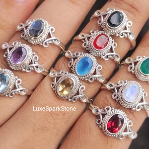 Könnte beinhalten: Eine Sammlung von Ringen aus Sterlingsilber mit ovalen Edelsteinen in verschiedenen Farben, darunter Blau, Rot, Grün und Lila. Die Ringe haben ein verziertes Design im Filigranstil um die Edelsteine.