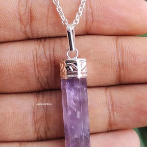 Könnte beinhalten: Eine silberne Halskette mit einem rechteckigen, lila Amethyst-Anhänger. Der Anhänger ist ein polierter Kristall mit einer silbernen Kappe. Die Kette ist eine filigrane Silberkette. Der Text "LuxeSparkStone" ist sichtbar.