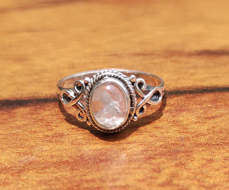 Pu&ograve; includere: Un anello d'argento con una gemma ovale di colore chiaro. La gemma &egrave; incastonata in una lunetta dettagliata con un motivo a corda intrecciata. L'anello presenta volute decorative sui lati, creando un aspetto elegante e ornato.