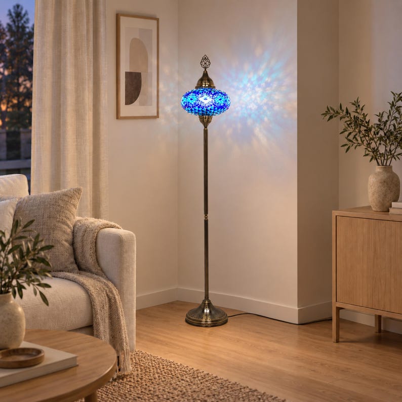 May include: A tall floor lamp featuring a round, blue mosaic glass shade with intricate patterns. The lamp has a slender, dark bronze-toned metal stand and a circular base. When illuminated, the shade casts a vibrant blue light pattern.