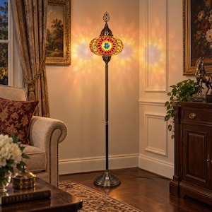 May include: A tall floor lamp featuring a round, multi-colored mosaic glass shade with intricate geometric patterns in red, yellow, blue, and green. The lamp has a slender, dark metal stand and a circular base, emitting a warm, glowing light.