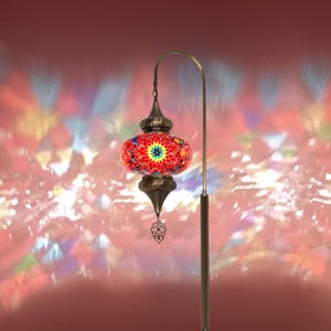May include: A decorative floor lamp with a mosaic glass shade. The shade is red with colourful mosaic pieces and a starburst design. The lamp has a bronze-coloured metal frame and a decorative hanging element. The lamp is approximately 152 cm tall.