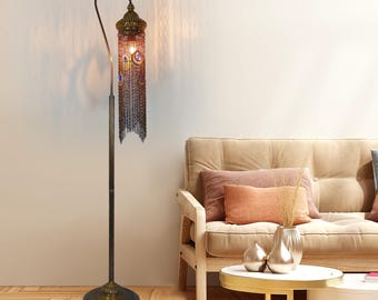 May include: A tall, ornate floor lamp with a bronze finish. The lamp features a decorative shade with hanging chain accents and jewel-toned embellishments. The lamp's base is round and textured, and the overall design has an antique or vintage aesthetic.