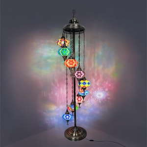 May include: A tall, ornate floor lamp with a bronze finish. The lamp features a series of colorful, mosaic glass globes suspended from chains. The globes are in various colors, including blue, green, red, and yellow, and cast a vibrant light.