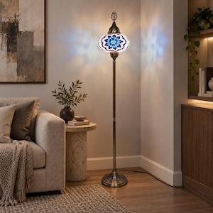 May include: A tall floor lamp featuring a brass-toned metal stand and a round base. The lamp has a decorative, globe-shaped shade crafted from blue and white mosaic glass pieces arranged in a star-like pattern, emitting a soft, ambient light.