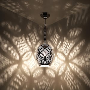 May include: A decorative pendant light fixture with an intricate, patterned metal shade. The light casts a complex pattern of shadows on the surrounding walls. The fixture hangs from a chain and ceiling mount, creating a warm, ambient glow.