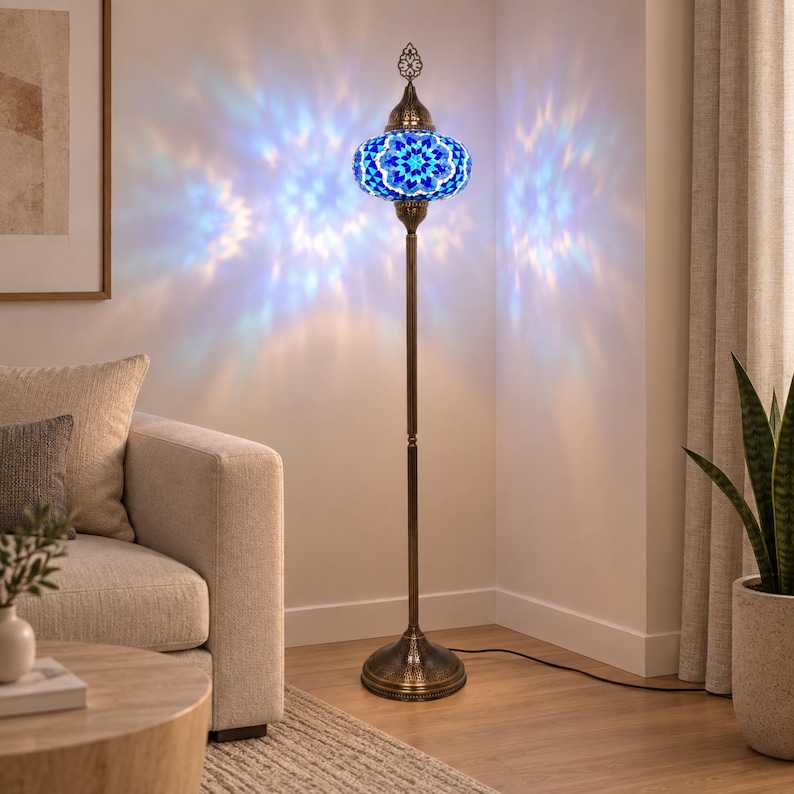 May include: A tall floor lamp with a bronze-colored metal stand and a round base. The lamp features a spherical shade crafted from blue and white mosaic glass pieces, casting intricate, star-shaped light patterns onto the surrounding walls.