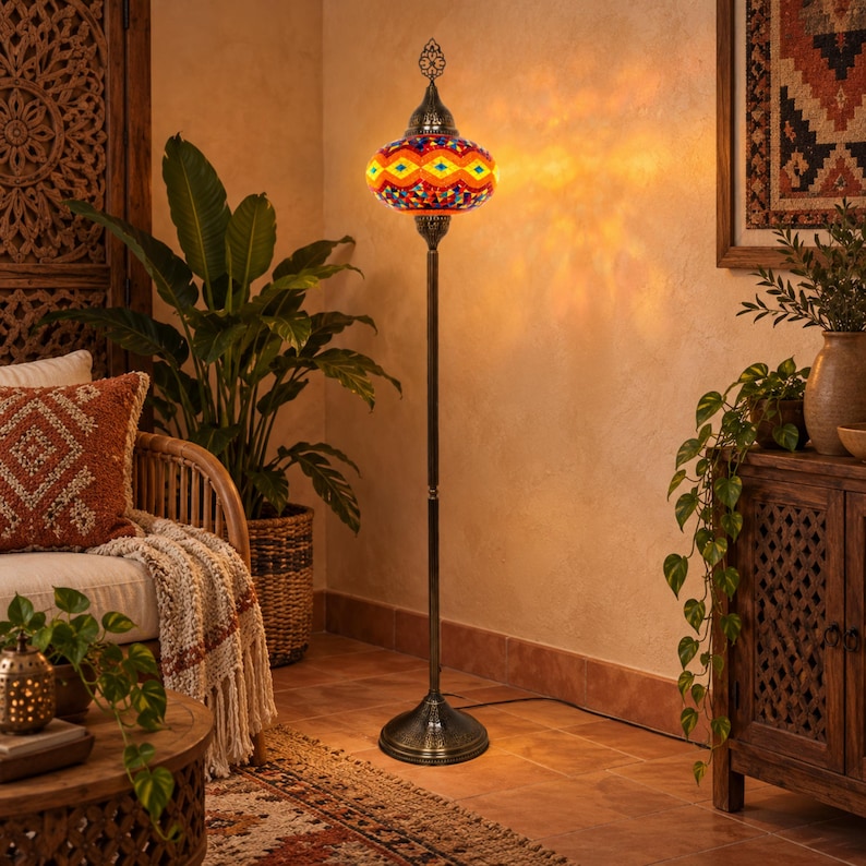 May include: A tall floor lamp featuring a vibrant, multi-colored mosaic glass shade with geometric patterns in orange, yellow, and blue. The lamp has a slender, dark metal stand and a circular base, emitting a warm, glowing light onto the wall.
