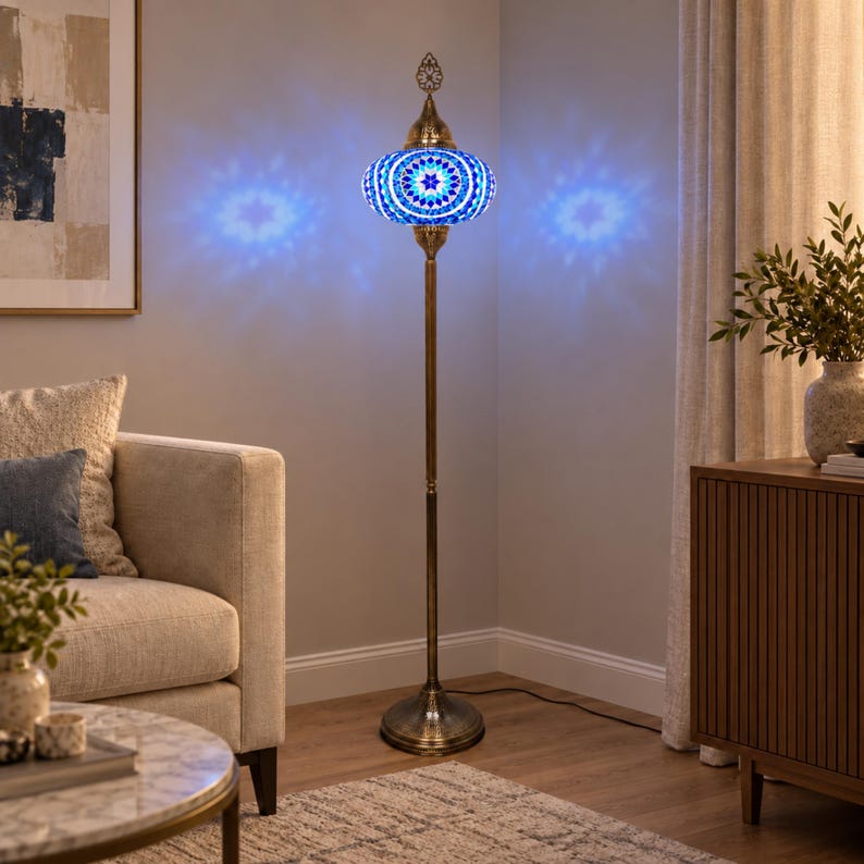 May include: A tall floor lamp featuring a brass-toned metal stand and a round, mosaic glass shade. The shade displays a geometric pattern in shades of blue and white, emitting a bright blue light that casts star-shaped patterns on the wall.