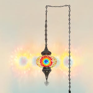 Könnte beinhalten: Eine hängende Mosaiklampe mit einem farbenfrohen, aufwendigen Design. Die Lampe weist eine lebendige Farbpalette auf, darunter Rot, Gelb, Blau und Grün. Sie wird von einer dekorativen Kette und einer Metallhalterung getragen, die jedem Raum Eleganz verleiht.