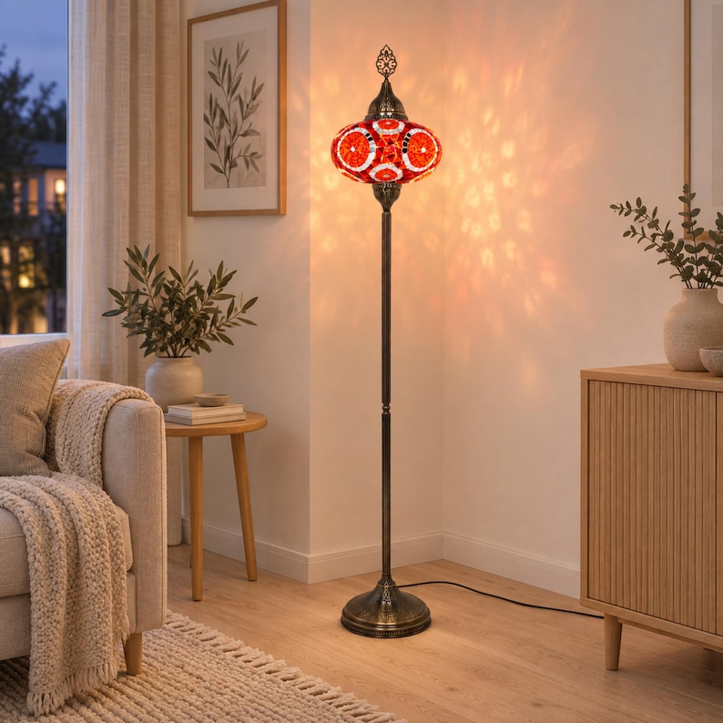 May include: A tall floor lamp featuring a round, mosaic glass shade in vibrant shades of red and orange. The lamp has a slender, dark metal stand with a circular base and a decorative metal finial at the top, emitting a warm, patterned glow.