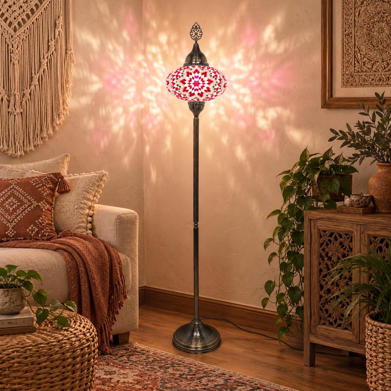 May include: A tall floor lamp featuring a round, mosaic glass shade with a red, white, and pink geometric floral pattern. The lamp has a slender, dark bronze-toned metal stand and a circular base, casting a warm, patterned light on the wall.