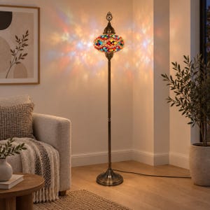 May include: A tall floor lamp featuring a multi-colored mosaic glass shade with a geometric pattern. The lamp has a slender, dark bronze-toned metal stand and a circular base, casting a vibrant, warm, and multi-colored light pattern on the wall.