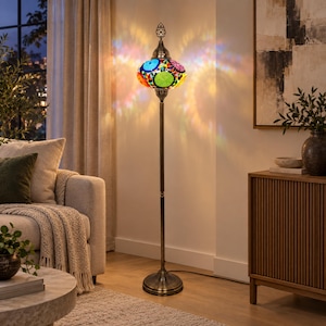 May include: A tall floor lamp with a slender bronze-toned metal stand and a circular base. The lamp features a spherical shade crafted from colorful mosaic glass pieces in shades of blue, green, red, and yellow, emitting a vibrant light pattern.