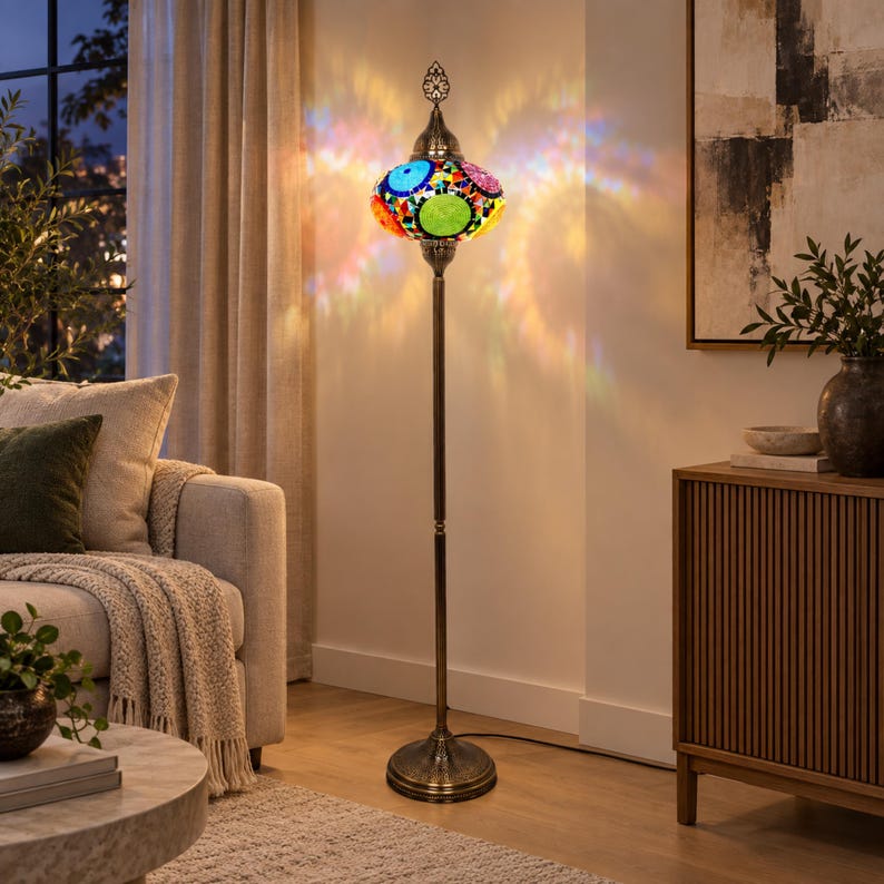 May include: A tall floor lamp with a slender bronze-toned metal stand and a circular base. The lamp features a spherical shade crafted from colorful mosaic glass pieces in shades of blue, green, red, and yellow, emitting a vibrant light pattern.