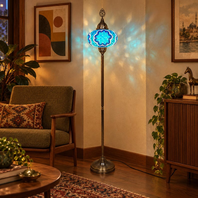 May include: A tall floor lamp featuring a mosaic glass shade in shades of blue and white with a star pattern. The lamp has a slender, dark metal stand and a circular base, casting a patterned light projection onto the surrounding wall surface.