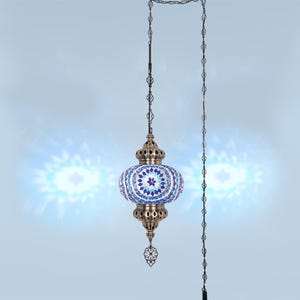 Puede incluir: Lámpara colgante con pantalla de mosaico de vidrio en tonos azules y blancos. La lámpara tiene un marco y una cadena de metal decorativos. La lámpara está suspendida de una cadena y un cable, diseñada para iluminación interior.