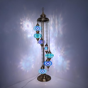May include: An elaborate floor lamp in a bronze finish, featuring multiple blue mosaic glass globes of varying sizes, suspended from chains. The lamp casts a patterned light on the wall.