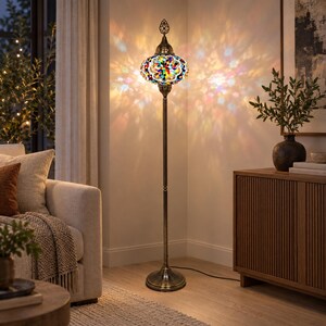 May include: A tall floor lamp featuring a multi-colored mosaic glass globe shade with intricate patterns. The lamp has a slender, antique brass-toned metal stand and a circular base, casting vibrant, multi-colored light patterns on the wall.