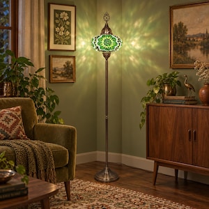 May include: A tall floor lamp featuring a mosaic glass shade in shades of green and white, mounted on a slender, dark metal stand with a circular base. The lamp emits a bright, patterned light that casts intricate shadows on the wall.