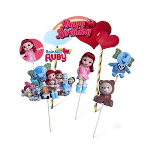 May include: Cake toppers featuring Rainbow Ruby characters, including Ruby dolls, a blue elephant, and a brown teddy bear. The toppers include a rainbow, red hearts, and the text "Happy Birthday".