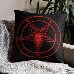 May include: Black square pillow featuring a red pentagram with a goat's head in the center. The design is encircled by a red ring with Hebrew letters and the number 7. The pillow is on a gray couch.