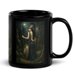 Puede incluir: Taza de cerámica negra con una ilustración detallada de una mujer en un bosque, sosteniendo una lanza y un escudo. La obra de arte representa una figura clásica con un búho y una luna llena en el fondo. La taza tiene un acabado brillante.