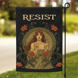 Può includere: Bandiera da giardino nera con la scritta "RESIST" in lettere dorate. La bandiera presenta un'illustrazione in stile Art Nouveau di una donna con i capelli rossi, circondata da fiori, che mostra il dito medio.