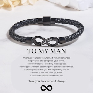 May include: Black braided leather bracelet with a black infinity charm. The charm has the names "Lisa" and "Henry" engraved. The text "TO MY MAN" is below the bracelet, along with a romantic message.