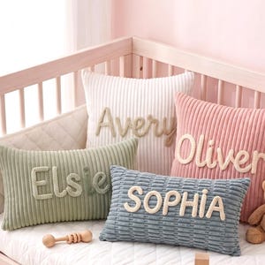 Puede incluir: Cuatro cojines de pana cuadrados y rectangulares en blanco, rosa, verde salvia y azul pizarra. Cada cojín presenta un nombre tejido en relieve en un color contrastante, con las inscripciones Avery, Oliver, Elsie y SOPHIA.