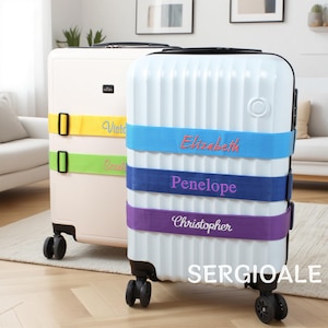 Könnte beinhalten: Zwei Rollkoffer, einer cremefarben und einer weiß, mit farbigen Namensbändern. Der weiße Koffer hat blaue, marineblaue und violette Bänder mit eingestickten Namen. Der cremefarbene Koffer hat gelbe und grüne Bänder mit Namen. Der Markenname "SERGIOALE" steht unten.