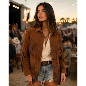 May include: A brown suede jacket featuring long fringe detailing across the chest and sleeves, a button-front closure, and a collar. The jacket is worn over a light-colored button-down shirt and blue denim shorts with a decorative belt buckle.