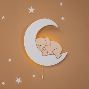 Moon-shaped wooden night light for baby nursery wall decor, sleeping baby moon lamp with warm LED glow, handcrafted plywood nursery light for toddler room, Montessori inspired baby room decoration, neutral beige crescent moon wall lamp with stars, soft ambient lighting for kids bedroom, Scandinavian style nursery decor for newborn and infant room.