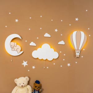 Wooden elephant on moon and hot air balloon night lights glowing on warm brown nursery wall, white cloud wall hanging and star stickers, clean wall display without crib, warm LED backlight on moon and balloon lamps, boho gender neutral nursery wall art set, handmade plywood moon cloud balloon decor, montessori style baby room wall light, toddler bedroom night light, scandinavian kids room decoration, baby shower gift idea