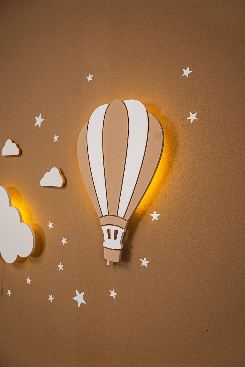 Close up of wooden hot air balloon night light with warm LED backlight glow, handmade plywood balloon wall lamp detail, white cloud and elephant moon decor partially visible, star stickers on warm brown nursery wall, natural wood texture and painted stripe detail on balloon lamp, boho nursery wall art, gender neutral baby room night light, montessori style kids bedroom wall decor, toddler room lamp, baby shower gift