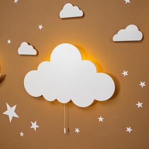 Cloud-shaped wooden night light for baby nursery wall decor, warm LED cloud lamp with hanging stars and clouds, Montessori inspired nursery lighting, neutral beige kids room decoration, handcrafted plywood night light for toddler bedroom, soft ambient nursery lamp for baby room, modern Scandinavian style wall light for children’s room.