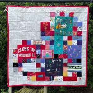 May include: A white quilt with a red border. The quilt is made of squares of different fabrics, including denim, flannel, and cotton. The squares are arranged in a random pattern. Some of the squares have embroidered designs, such as flowers and a hot dog on skis. The quilt also includes patches with text, such as "Close Up Washington, D.C." and "Park City Utah".