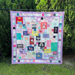 May include: A purple and white patchwork quilt with a variety of colorful squares featuring different designs and text. The text includes "Walrus", "Gap", "All You Need Is Love", "Taquito", "First", and "1000".