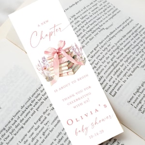 May include: A bookmark with a watercolor design for a baby shower. The bookmark features a stack of books tied with a pink ribbon, lavender sprigs, and the text "A New Chapter" and "Olivia's baby shower".