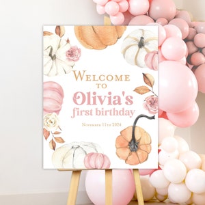 May include: Welcome to Olivia's first birthday sign featuring a watercolour design with pumpkins, leaves, and flowers in shades of pink, orange, and white. The sign also includes the date "November 11th 2024".