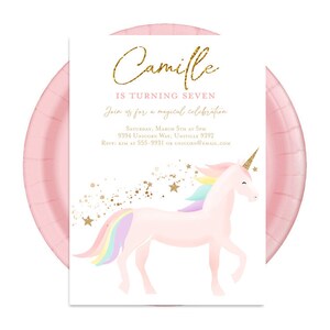 May include: Pink invitation with gold glitter text that reads "Camille is turning seven. Join us for a magical celebration. Saturday, March 17th at 3pm. 9394 Unicorn Way, Univille 9192. RSVP at 555-9931 or unicorn@email.com". The invitation features a pink unicorn with a rainbow mane and tail against a white background with gold glitter stars.