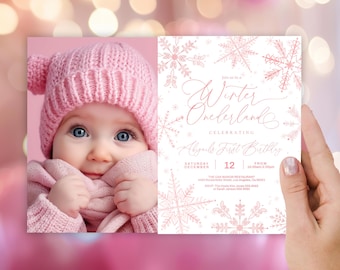 May include: A pink and white winter wonderland themed first birthday party invitation with a photo of a baby girl wearing a pink hat and scarf. The invitation text reads "Join us in a Winter Wonderland Celebrating [baby's name] First Birthday".