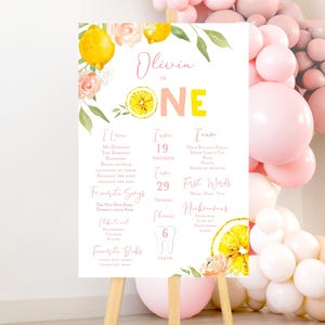 Könnte beinhalten: Ein personalisiertes Geburtstags-Schild für Olivia, ein einjähriges Mädchen, mit einem Zitronen- und Blumendesign. Das Schild enthält Informationen über die Vorlieben des Kindes, Maße, Lieblingslieder und erste Worte. Auf einem Holzstaffelei ausgestellt.